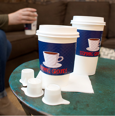 Two paper coffee cups with custom printed sleeves on a table with napkins and small cream packages.