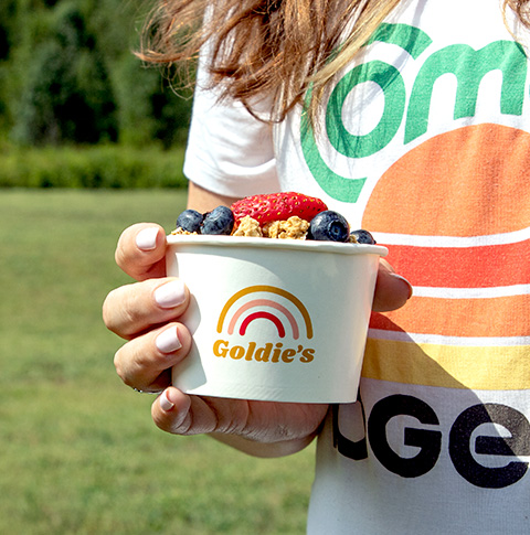 A hand holding a custom printed food cup full of fruit and granola with a "Goldie's" logo.