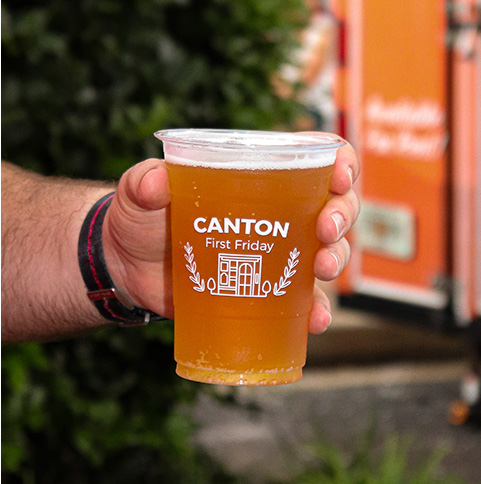 A hand holds a plastic cup with custom "Canton First Friday" logo.