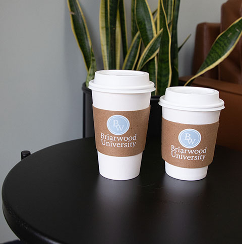 Two paper hot cups with kraft sleeves labeled with "Briarwood University" logo.